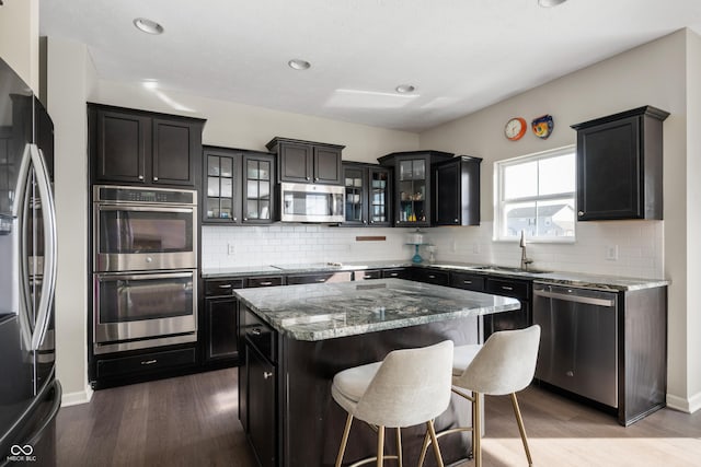 kitchen with stone counters, sink, hardwood / wood-style flooring, a center island, and stainless steel appliances