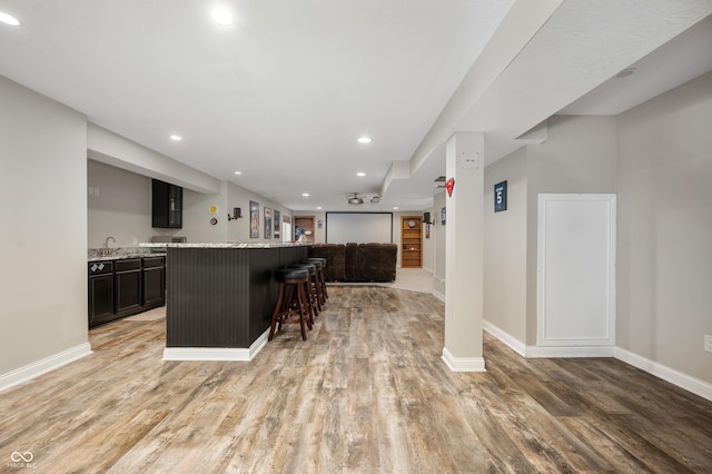 kitchen with light stone counters, a kitchen island, a kitchen breakfast bar, and light hardwood / wood-style flooring