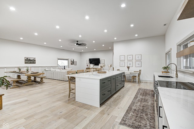 kitchen with a breakfast bar, sink, stainless steel range with electric stovetop, light hardwood / wood-style floors, and light stone counters