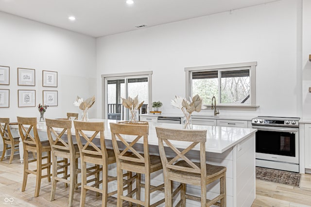 kitchen featuring a breakfast bar, white cabinetry, stainless steel electric range oven, a center island, and light wood-type flooring