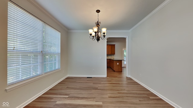 unfurnished dining area with crown molding, a healthy amount of sunlight, an inviting chandelier, and light hardwood / wood-style flooring