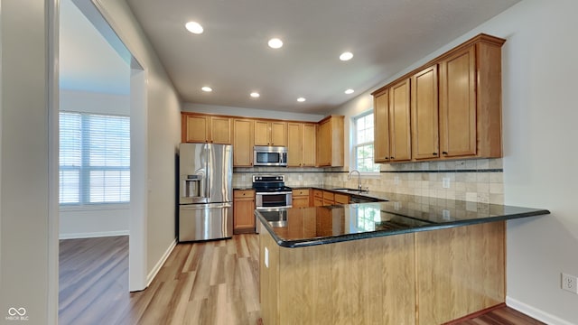 kitchen with stainless steel appliances, light wood-type flooring, dark stone counters, and kitchen peninsula