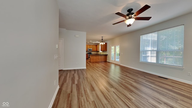 unfurnished living room with ceiling fan with notable chandelier and light hardwood / wood-style floors