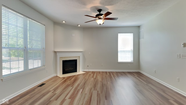 unfurnished living room with ceiling fan, a textured ceiling, and light hardwood / wood-style flooring