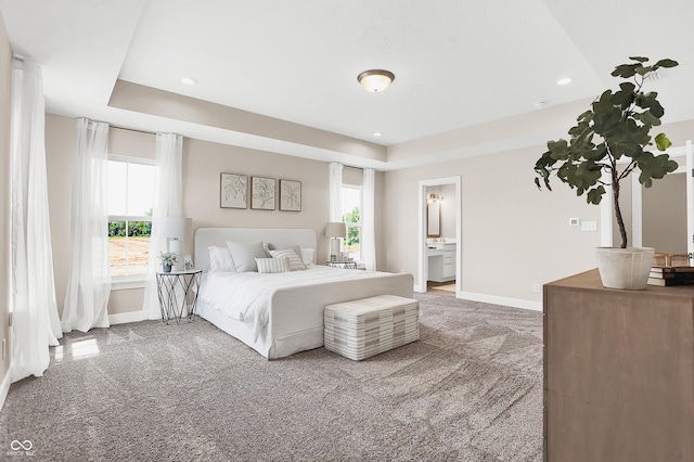 carpeted bedroom featuring ensuite bathroom, a raised ceiling, and multiple windows