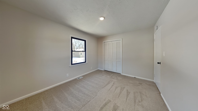 unfurnished bedroom featuring light carpet, a closet, and a textured ceiling