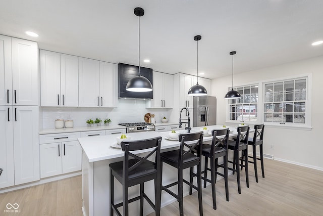 kitchen featuring appliances with stainless steel finishes, a kitchen island with sink, white cabinets, and decorative light fixtures