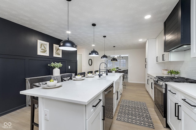 kitchen with a breakfast bar, white cabinetry, appliances with stainless steel finishes, an island with sink, and pendant lighting