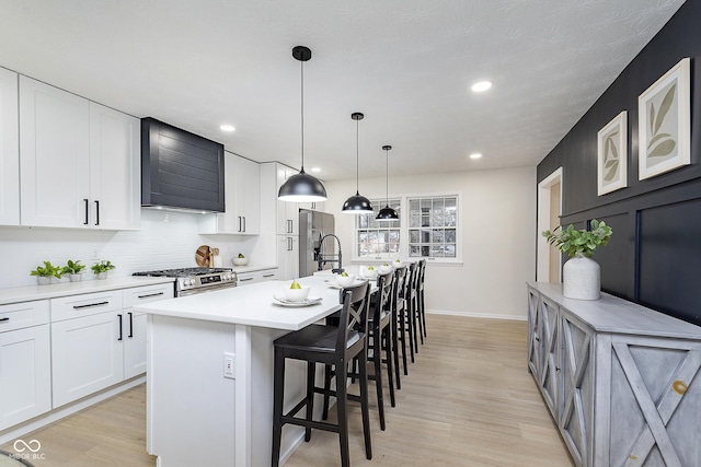 kitchen with wall chimney exhaust hood, white cabinetry, appliances with stainless steel finishes, a kitchen breakfast bar, and a kitchen island with sink