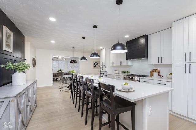 kitchen featuring wall chimney exhaust hood, stainless steel range with gas stovetop, decorative light fixtures, and white cabinets