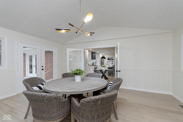 dining space with lofted ceiling, a chandelier, light hardwood / wood-style floors, and french doors