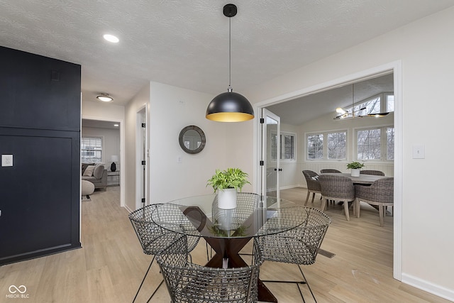 dining space with vaulted ceiling, light hardwood / wood-style floors, a chandelier, and a textured ceiling