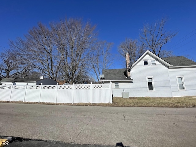 view of home's exterior featuring fence, roof with shingles, and a chimney