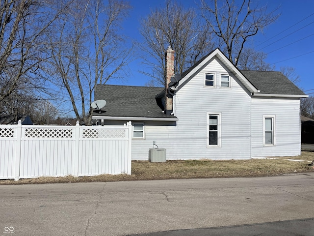 view of side of property with roof with shingles, central AC, a chimney, and fence