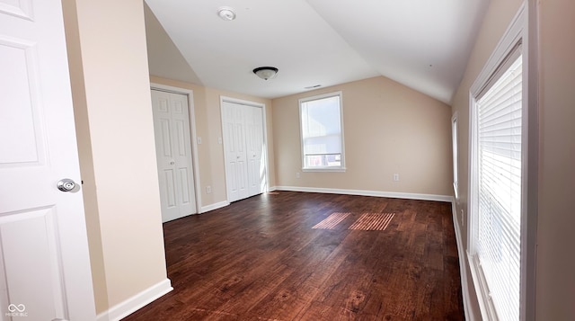 unfurnished bedroom featuring vaulted ceiling, dark hardwood / wood-style floors, and multiple closets