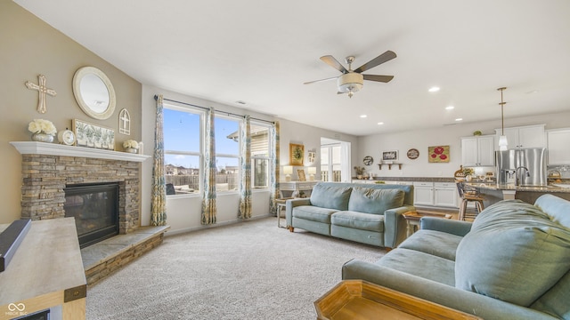 living room with ceiling fan, a stone fireplace, and light carpet