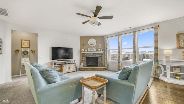 living room with ceiling fan, a stone fireplace, and hardwood / wood-style floors