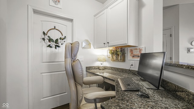 kitchen featuring built in desk, dark stone counters, and white cabinets