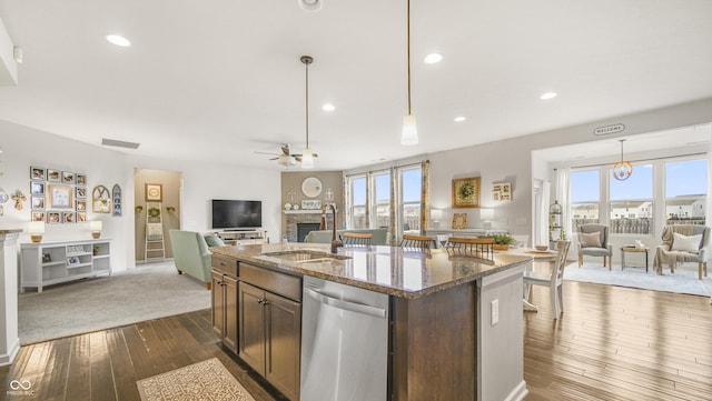 kitchen featuring sink, hanging light fixtures, a center island with sink, dishwasher, and dark stone counters