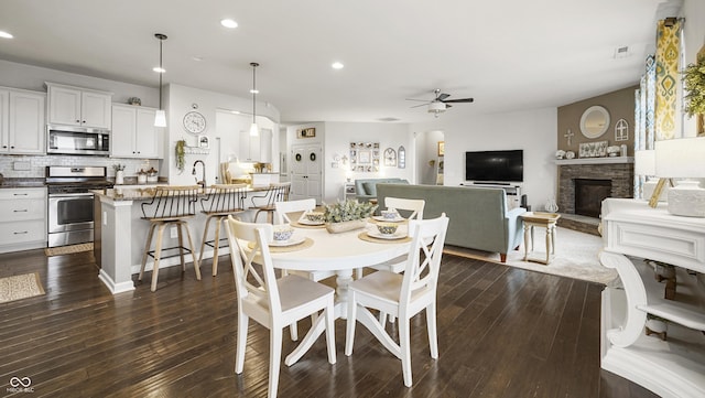 dining area featuring dark hardwood / wood-style floors, sink, a fireplace, and ceiling fan