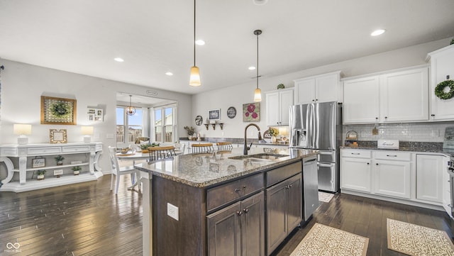 kitchen featuring pendant lighting, sink, dark stone countertops, white cabinets, and stainless steel fridge with ice dispenser