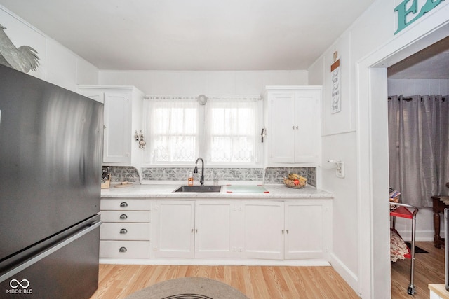 kitchen with white cabinetry, sink, stainless steel refrigerator, and light hardwood / wood-style flooring