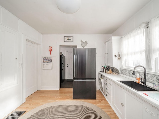 kitchen featuring stainless steel fridge, sink, light hardwood / wood-style flooring, and white cabinets