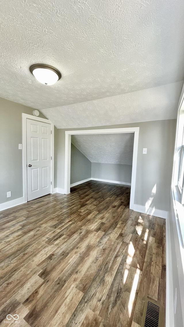 additional living space with lofted ceiling, dark wood-type flooring, and a textured ceiling