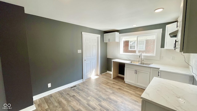 kitchen with sink, white cabinetry, ventilation hood, light hardwood / wood-style floors, and light stone countertops