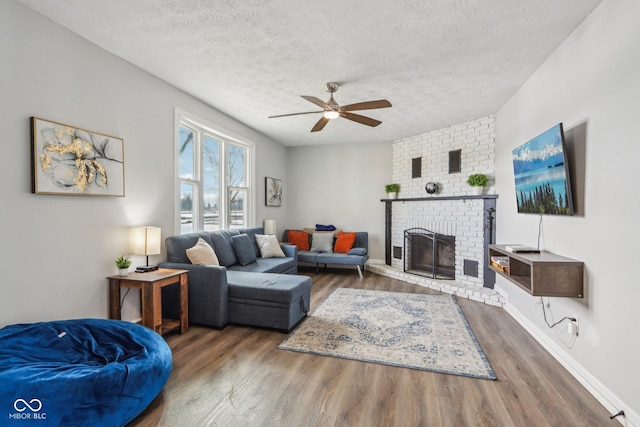 living room featuring dark wood-type flooring, ceiling fan, a fireplace, and a textured ceiling