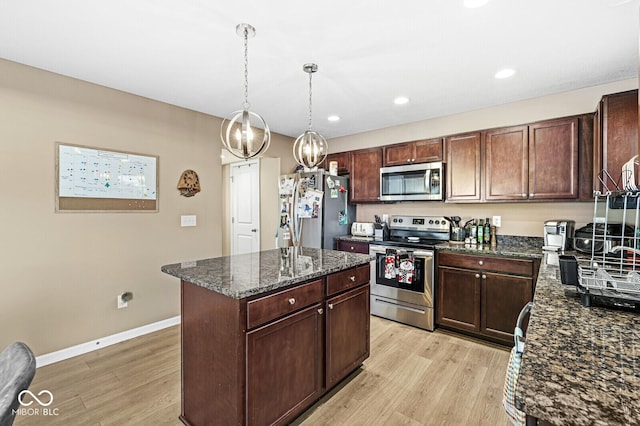 kitchen with a center island, light wood-type flooring, dark stone countertops, appliances with stainless steel finishes, and pendant lighting