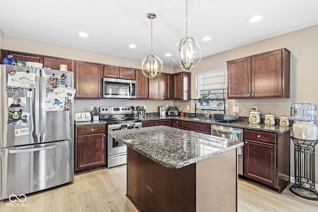 kitchen with appliances with stainless steel finishes, a center island, light hardwood / wood-style floors, and hanging light fixtures