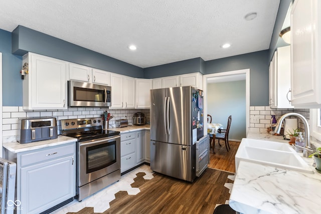 kitchen with appliances with stainless steel finishes, sink, white cabinets, dark hardwood / wood-style flooring, and decorative backsplash