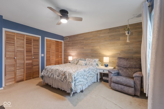 carpeted bedroom featuring ceiling fan, multiple closets, and wood walls