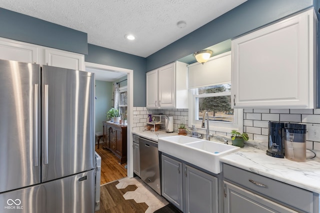 kitchen featuring sink, gray cabinets, white cabinetry, stainless steel appliances, and light stone counters