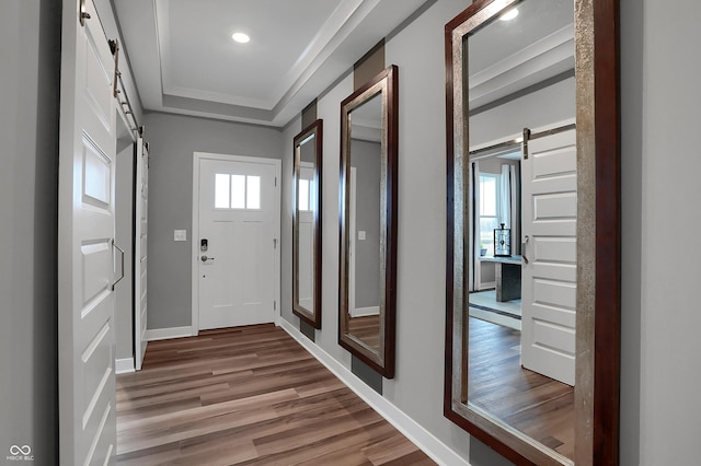 entryway featuring a tray ceiling, wood-type flooring, ornamental molding, and a barn door