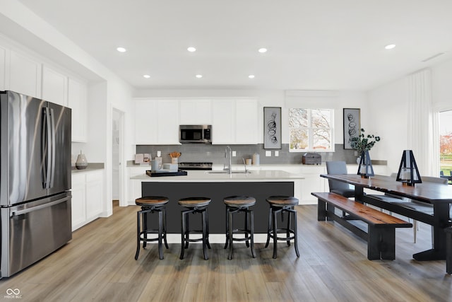 kitchen featuring appliances with stainless steel finishes, tasteful backsplash, sink, white cabinets, and a center island with sink