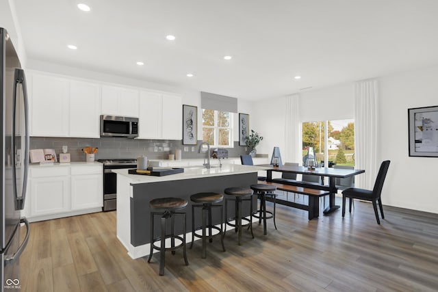 kitchen featuring appliances with stainless steel finishes, tasteful backsplash, white cabinetry, sink, and a center island with sink