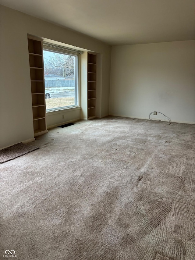 unfurnished room with built in shelves and light carpet