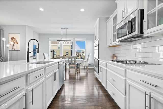 kitchen with sink, white cabinets, backsplash, hanging light fixtures, and stainless steel appliances