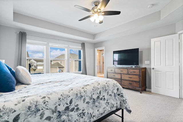 bedroom featuring ceiling fan, light colored carpet, a raised ceiling, and ensuite bath