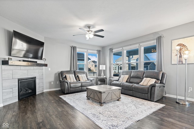 living room with ceiling fan, dark hardwood / wood-style flooring, a tiled fireplace, and a textured ceiling