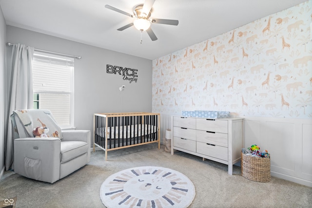 carpeted bedroom with a crib and ceiling fan