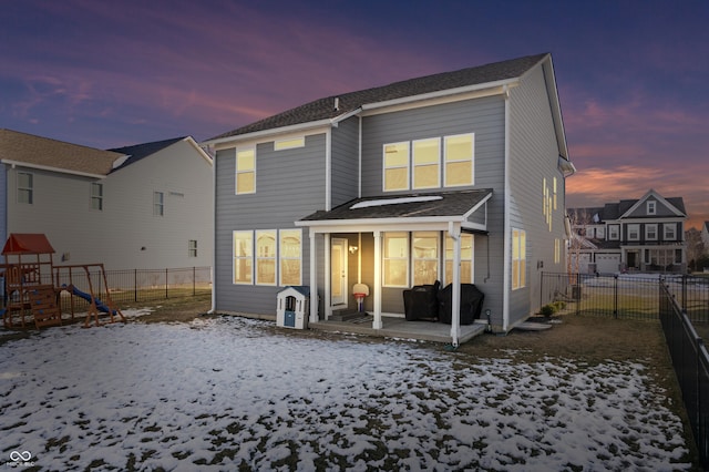 snow covered back of property featuring a playground and a sunroom