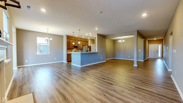 unfurnished living room with an inviting chandelier, a textured ceiling, and hardwood / wood-style flooring