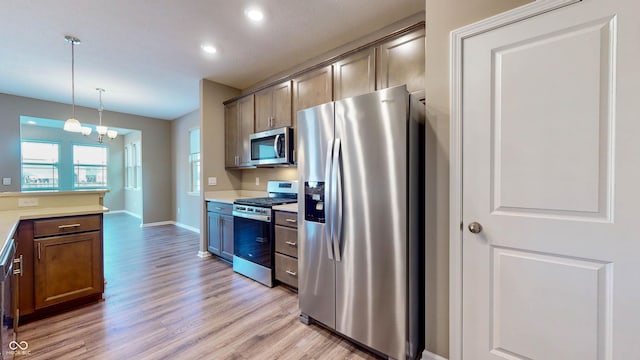 kitchen with appliances with stainless steel finishes, an inviting chandelier, light wood-type flooring, and decorative light fixtures