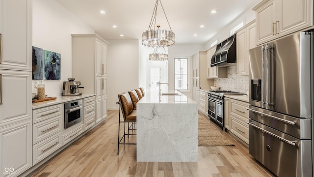 kitchen featuring a kitchen island with sink, hanging light fixtures, high end appliances, light stone counters, and exhaust hood