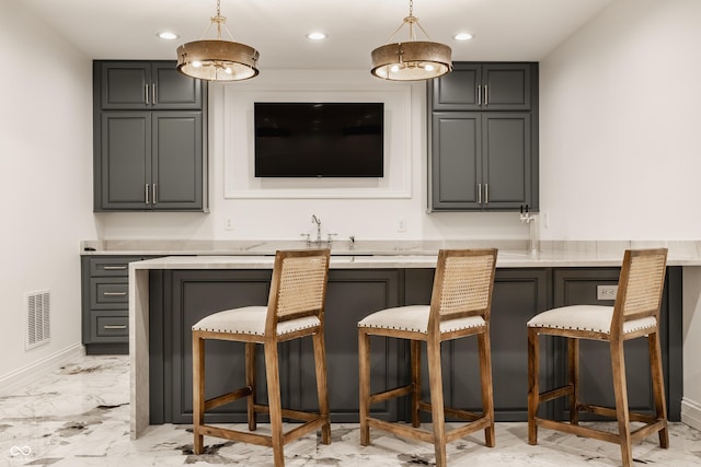 bar with gray cabinets, light stone countertops, and pendant lighting