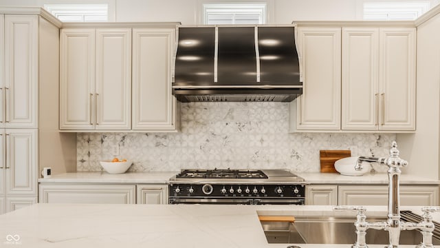 kitchen featuring extractor fan, decorative backsplash, range with two ovens, light stone countertops, and cream cabinets