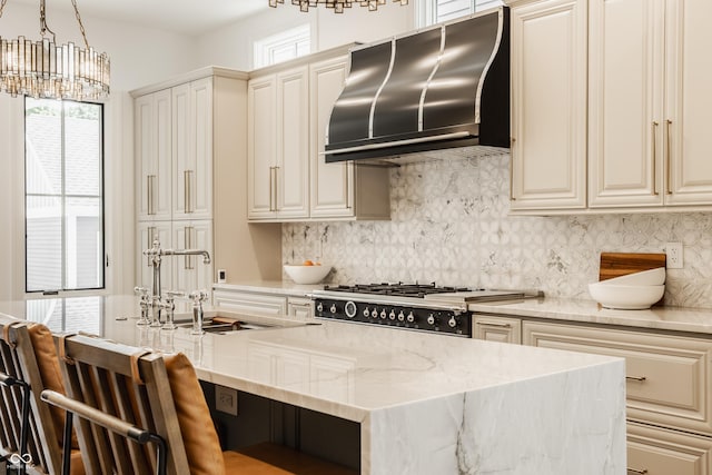 kitchen featuring pendant lighting, wall chimney exhaust hood, light stone counters, plenty of natural light, and cream cabinetry